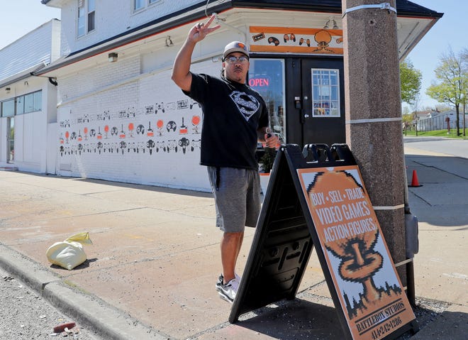 Bryant Wilcox, Battlebox Studios co-owner, waves to a motorist blowing their horn while he puts out a sign after reopening the family-owned gaming store at 5431 W. Lisbon Ave. in Milwaukee on Tuesday, May 12, 2020.  As of May 11, standalone or strip mall-based retail stores can offer in-person shopping, as long as customers are limited to five at a time and social-distancing guidelines are followed, Gov. Tony Evers announced Monday.