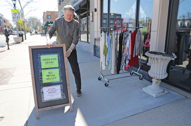 Michael Kruczynski, owner of New Options Salon and Boutique, places a sign on the sidewalk shortly after reopening his shop on East Silver Spring Drive in Whitefish Bay on Tuesday.  As of Monday, stand-alone or strip mall-based retail stores can offer in-person shopping, as long as customers are limited to five at a time and social-distancing guidelines are followed, Gov. Tony Evers announced.
