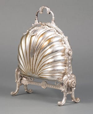 This silver-plated serving piece is called a box but it doesn't look like one. It held English biscuits, but if the sides opened, the cookies inside would fall down. Each of the shell-shaped bowls had a hinged, pierced flap that kept the heat and the biscuits in place when the sides were opened and became flat bowls to serve the cookies. The flaps are often missing when the biscuit box is sold.